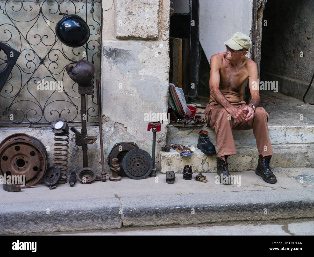 Ein Mann mittleren Alters kubanischen sitzt auf der vorderen Stoop seines Hauses Verkauf verwendet Autoteile in Havanna, Kuba. Stockfoto