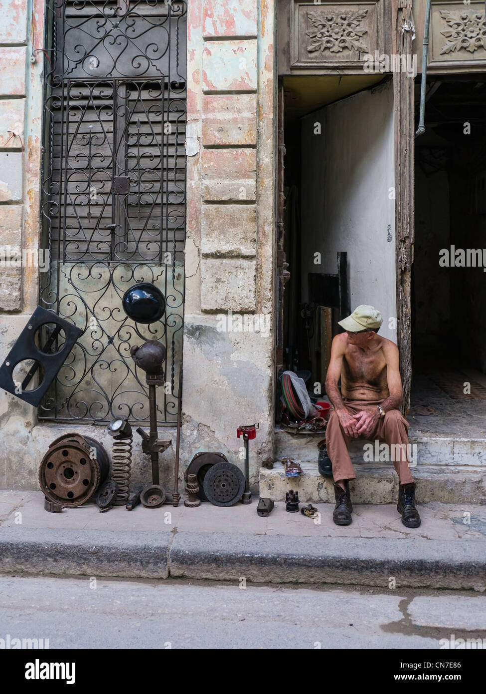 Ein Mann mittleren Alters kubanischen sitzt auf der vorderen Stoop seines Hauses Verkauf verwendet Autoteile in Havanna, Kuba. Stockfoto