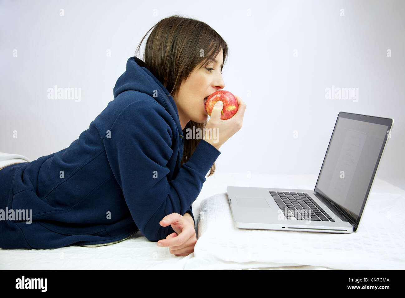 Frau glücklich Essen einen Apfel vor Computer im Bett Stockfoto