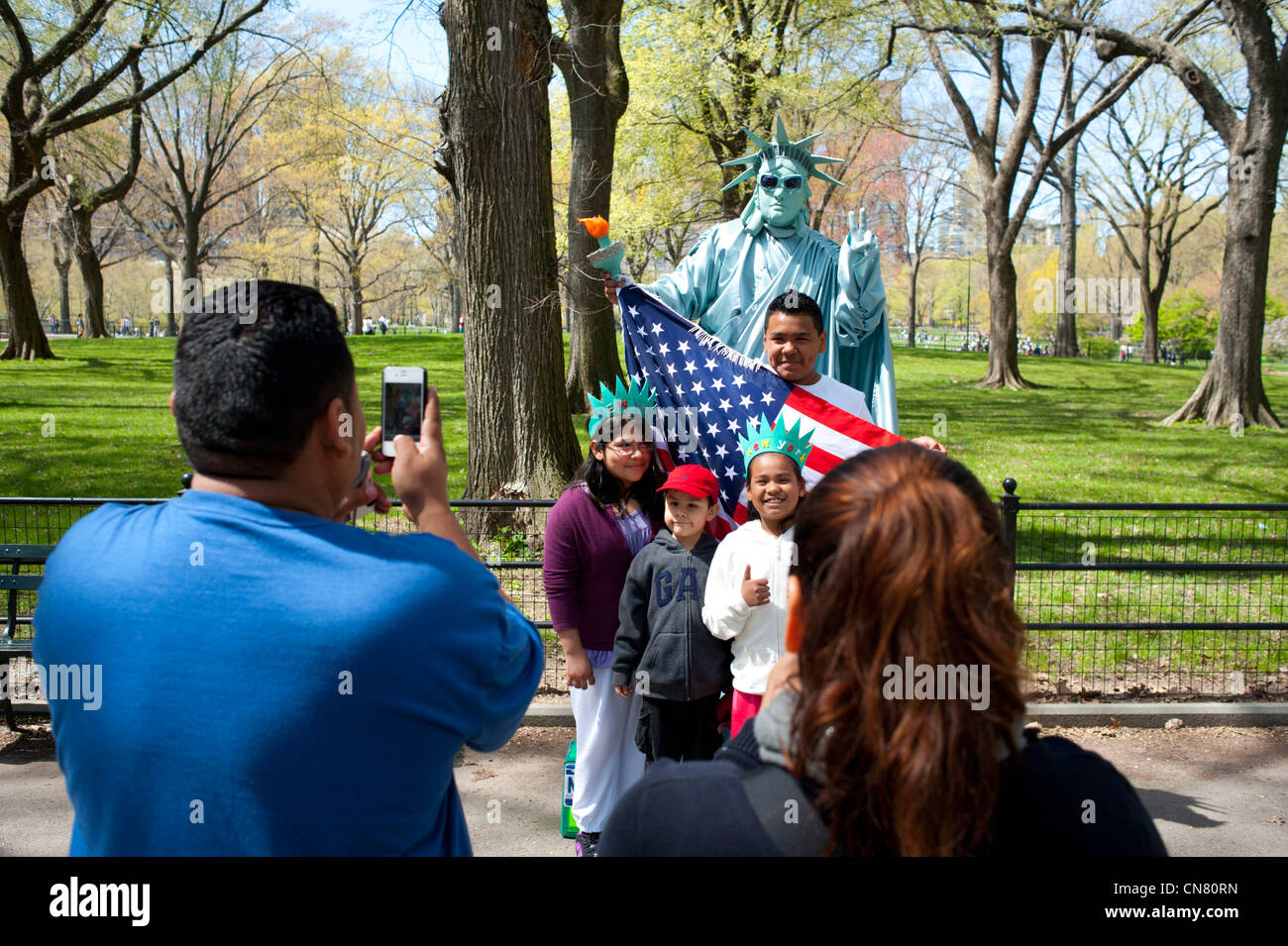 USA New York City NYC NY Manhattan Central Park - hispanischen Familie Posen mit einer menschlichen Statue of Liberty-amerikanische Flagge Stockfoto
