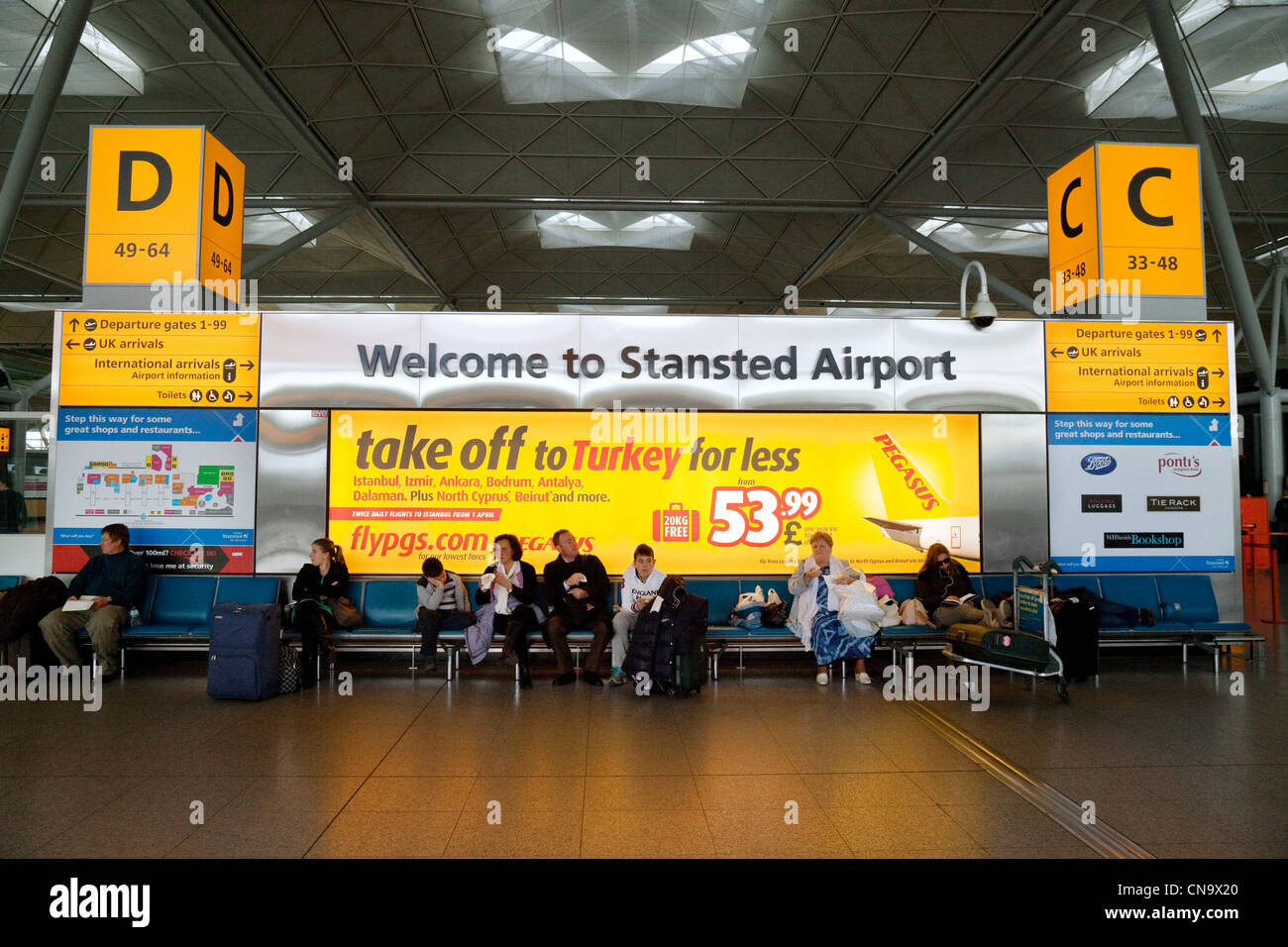 Willkommen bei Stansted Flughafen Zeichen in das Innere des Terminals sitzen Passagiere Stockfoto