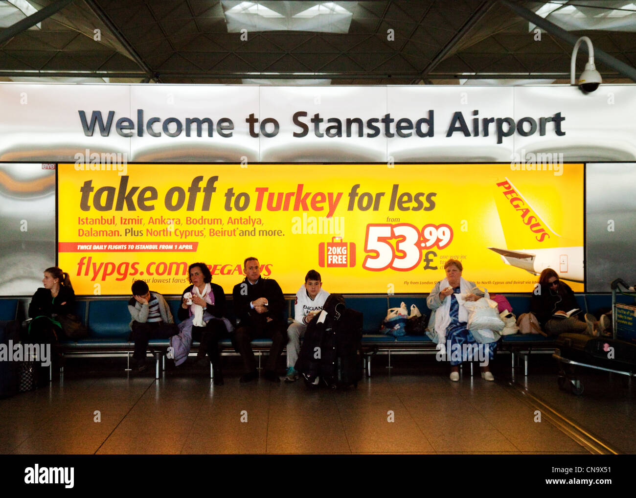 Willkommen bei Stansted Flughafen Zeichen in das Innere des Terminals sitzen Passagiere Stockfoto