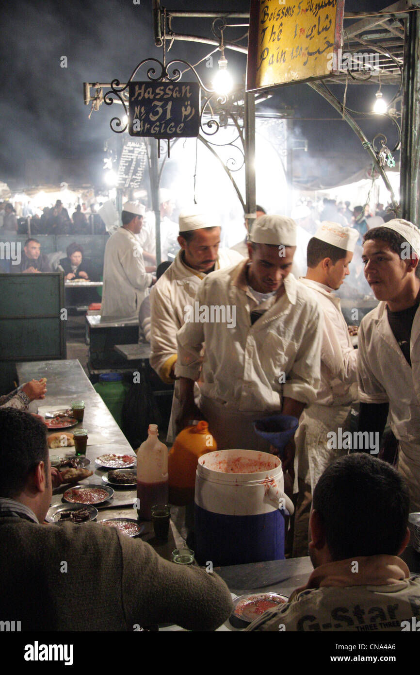 Menschen Essen an einem belebten Grill wo Essen über offenem Feuer im Herzen des Djemaa el Fna, Marrakesch, Marokko von Köchen zubereitet, Stockfoto