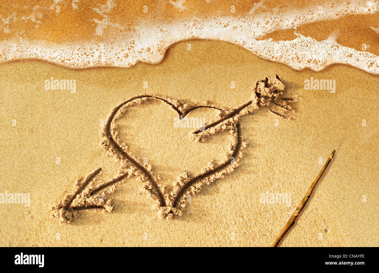 Herz mit Pfeil, als Zeichen der Liebe, direkt am Strand, mit etwas Wasser und Schaum aus dem Meer gezogen. Stockfoto