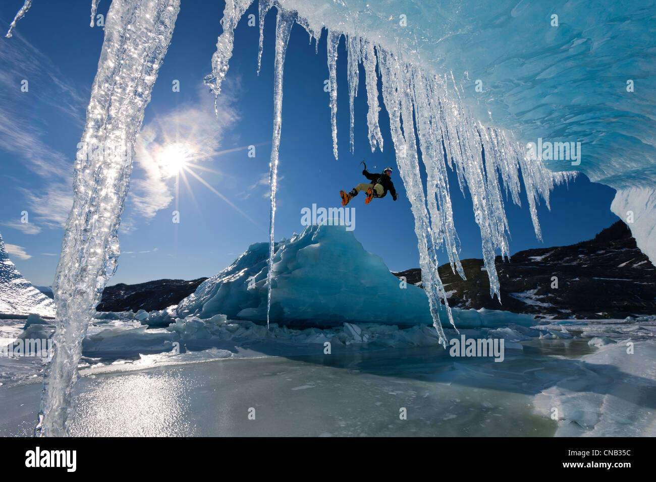 Zusammensetzung: Sonne scheint durch Eiszapfen hängen an einem Eisberg als ein Eiskletterer Abseilen über den Rand, Mendenhall Alaska Stockfoto