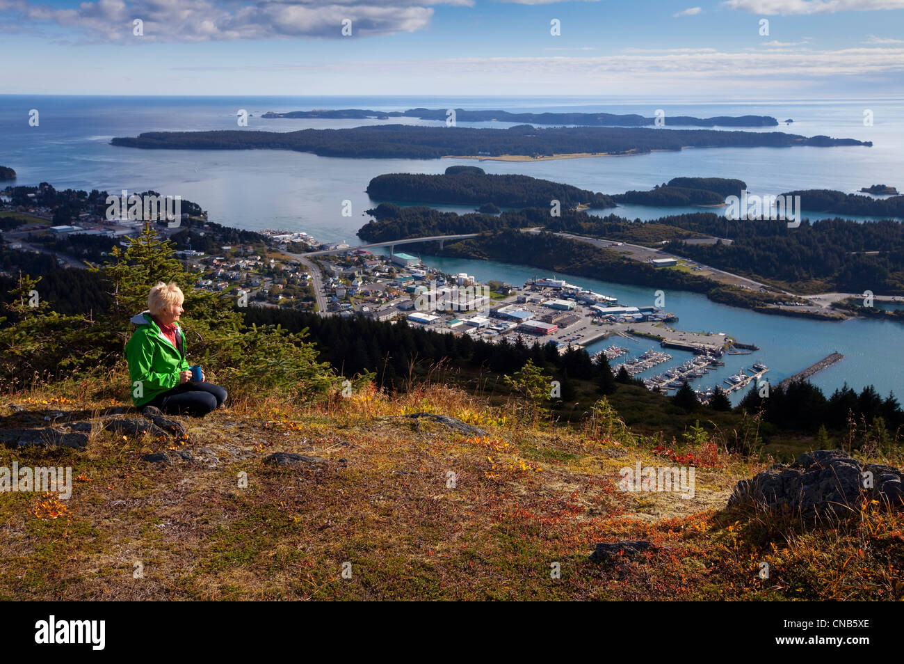 Reife Frau entspannt sich und genießt die Aussicht auf die Innenstadt Kodiak auf Säule Berg, Herbst, Südwest-Alaska, Kodiak Island Stockfoto