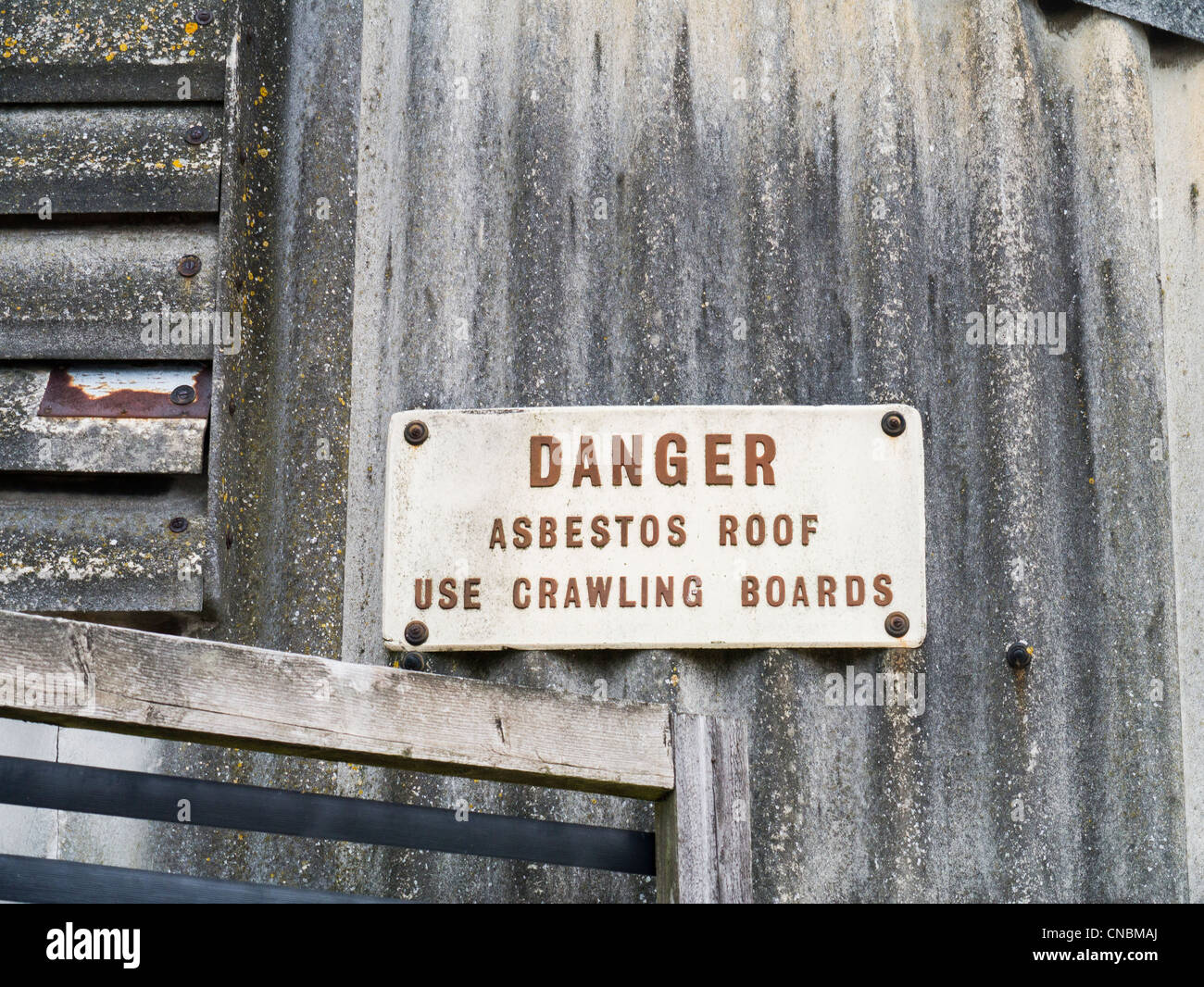Gefahrenzeichen auf einem industriellen Gebäude mit gewellten Asbest Dach und Wand Stockfoto