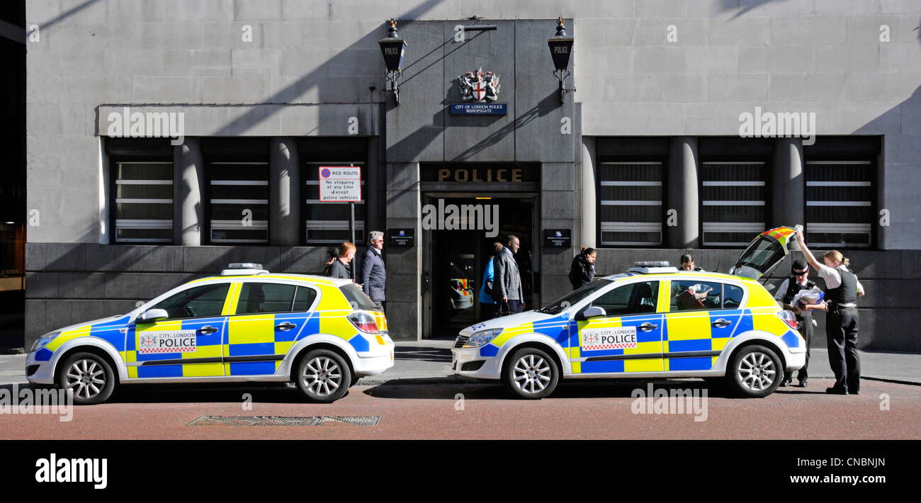 Polizeibeamte in Uniform neben geparkten Polizeiautos außerhalb der City of London Bishopsgate Polizeistation Eingang & blaue Lampen & unverbundene Passanten Stockfoto