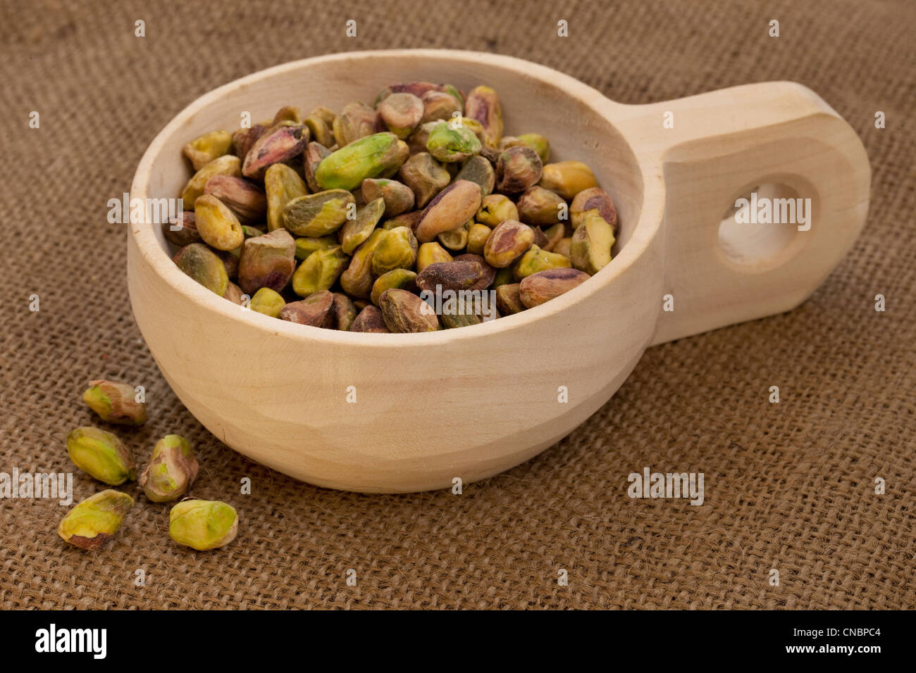 Rohe geschälte Pistazien auf eine rustikale, hölzerne Schaufel mit braunen Sackleinen Hintergrund Stockfoto