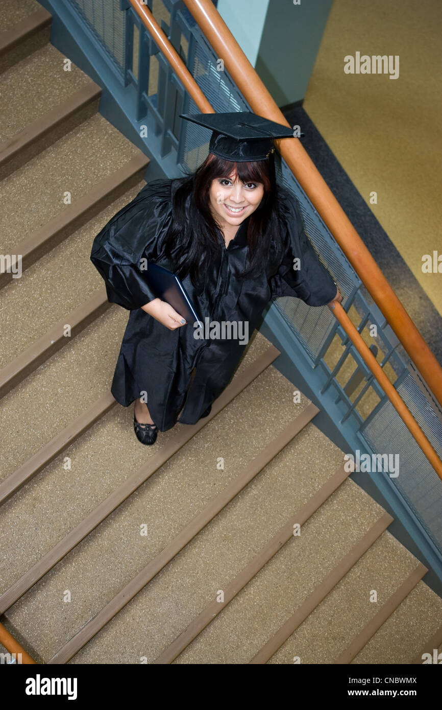 Hochschulabsolvent stellt auf einer Treppe mit dem Diplom in der hand. Stockfoto