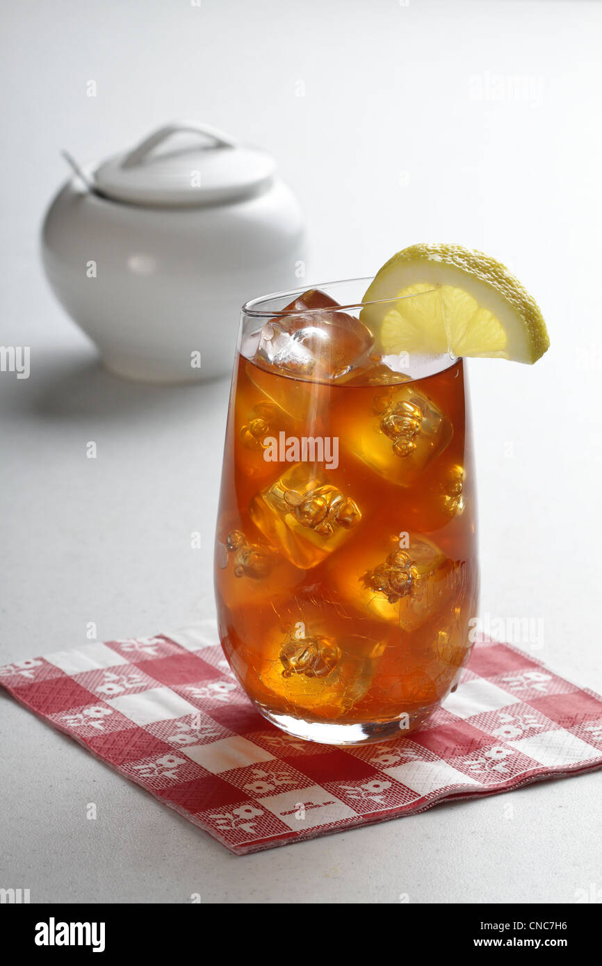 Ein Glas Eistee mit Zitronenscheibe auf einer karierten Serviette mit weißen Zuckerdose mit Löffel im Hintergrund. Stockfoto