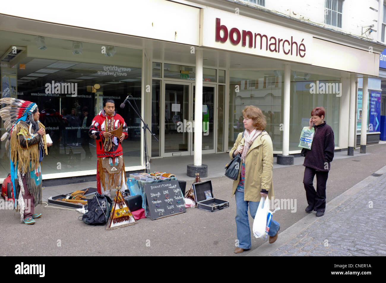 Südamerikanische Straßenmusikanten und Verkauf Schmuck als Straßenmusikant vor einem stillgelegten Geschäft in Falmouth, Cornwall Stockfoto