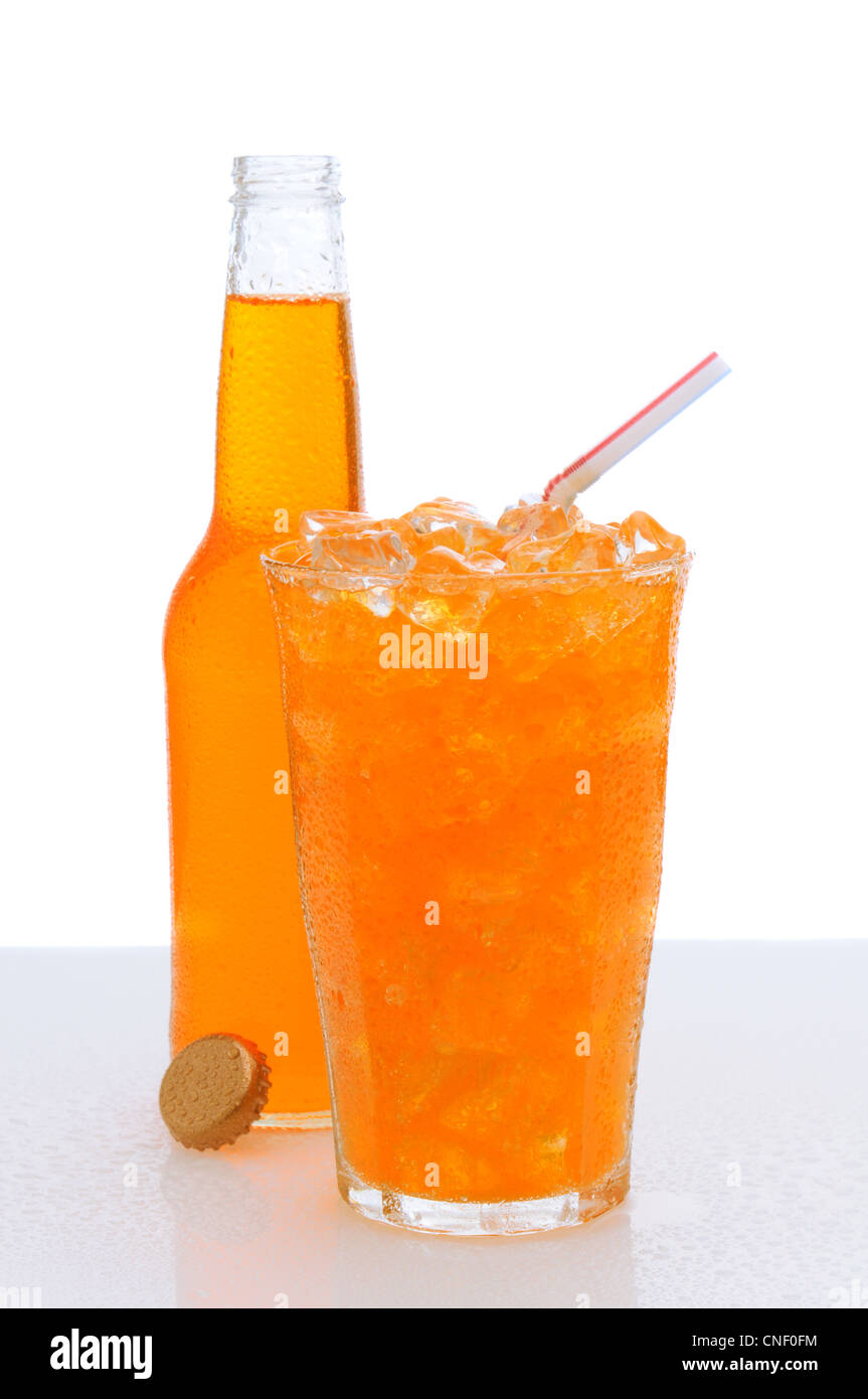 Ein kaltes Glas Orangenlimonade gefüllt mit Eis und einen Trinkhalm mit einer Flasche versteckt hinter. Stockfoto