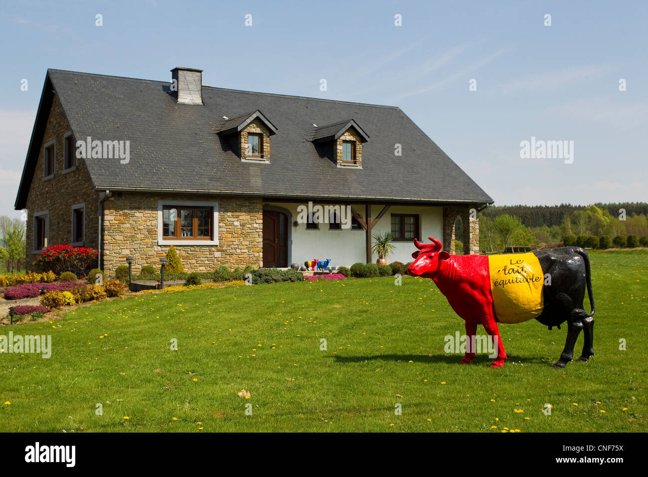 Ein rot, gelb und Schwarz bemalte Kuh stehend auf einer Wiese vor einem Bungalow. Stockfoto