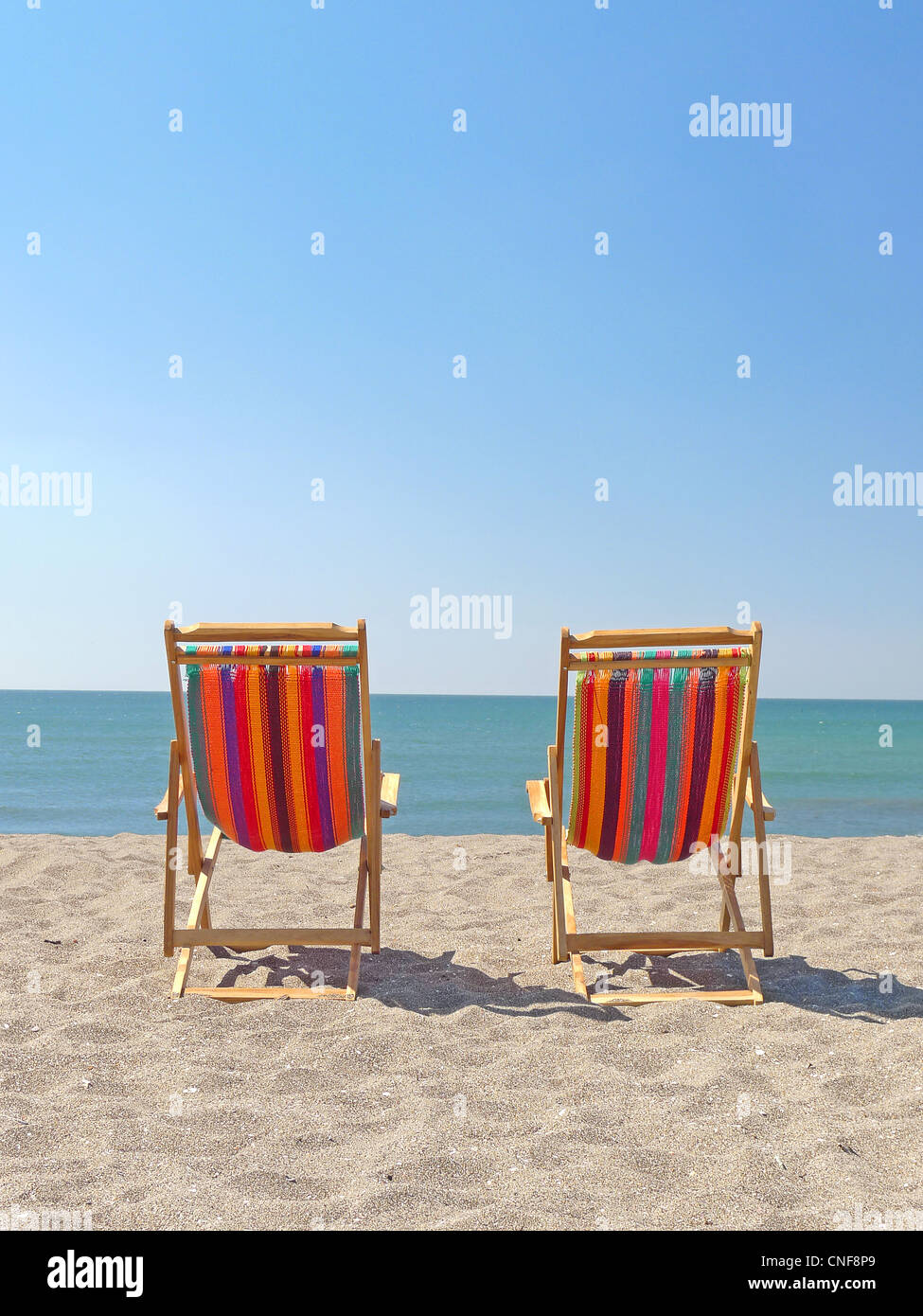 Zwei Stühle auf Sandstrand sonnigen Sommer Tag blauer Himmel glasklaren Meer Küste Ansicht Textfreiraum Stockfoto