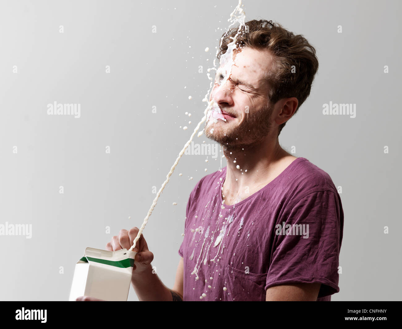 Junger Mann verschütten Milch aus Karton, Studio gedreht Stockfoto
