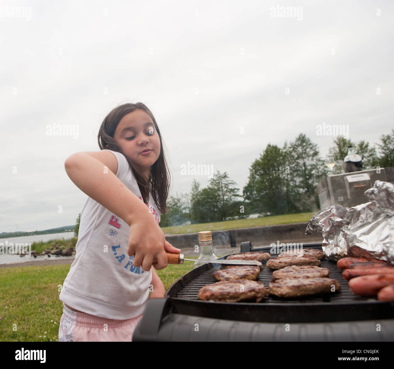 Junges Mädchen Braten Hamburger auf eine Bar b que. Kochen im Freien, essen Fleisch, Herd, Gasbrenner, Würstchen, Barbie, Sommer, outdoor, ute Stockfoto