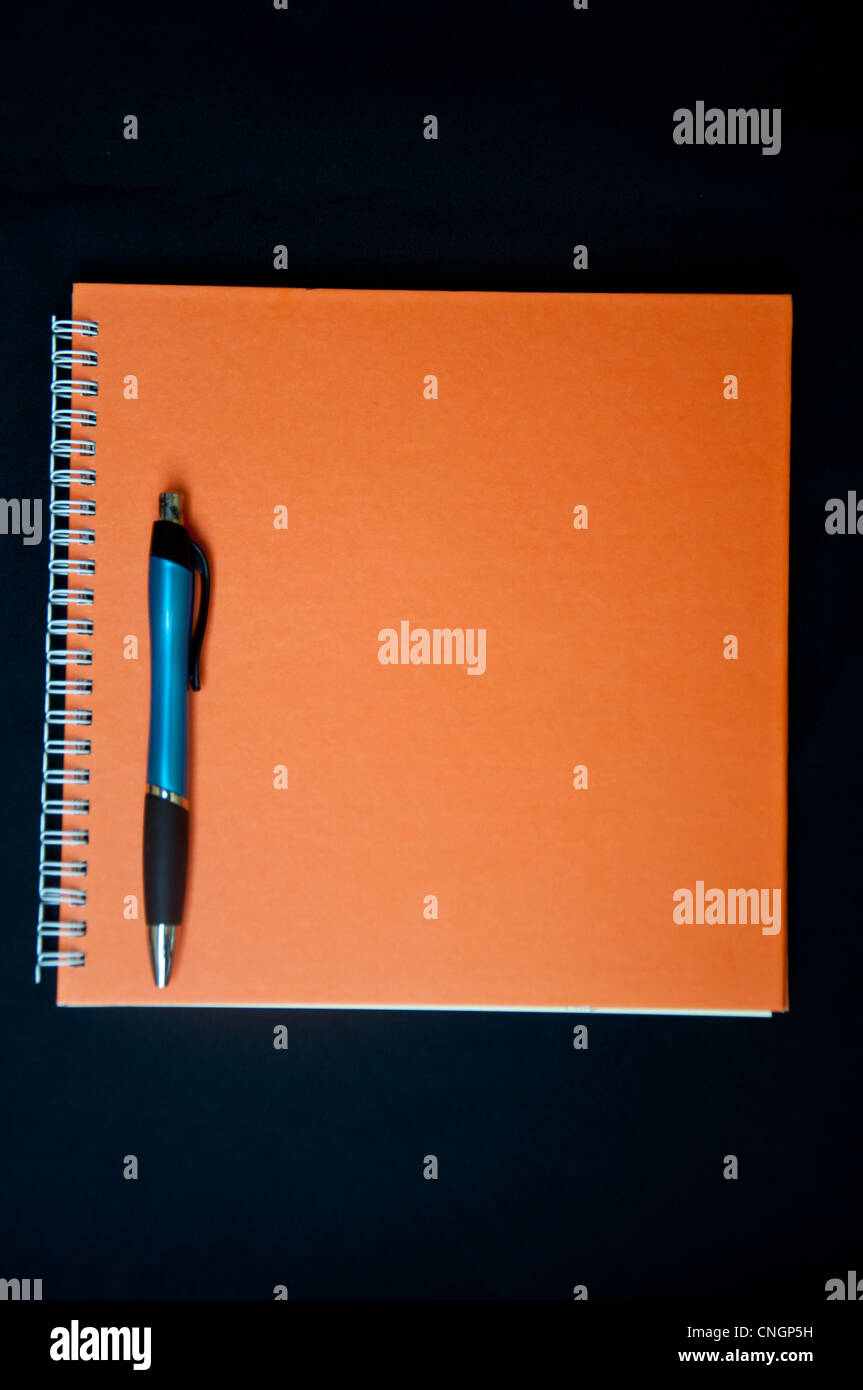 Orange Notizbuch und Stift auf schwarzem Hintergrund Stockfoto