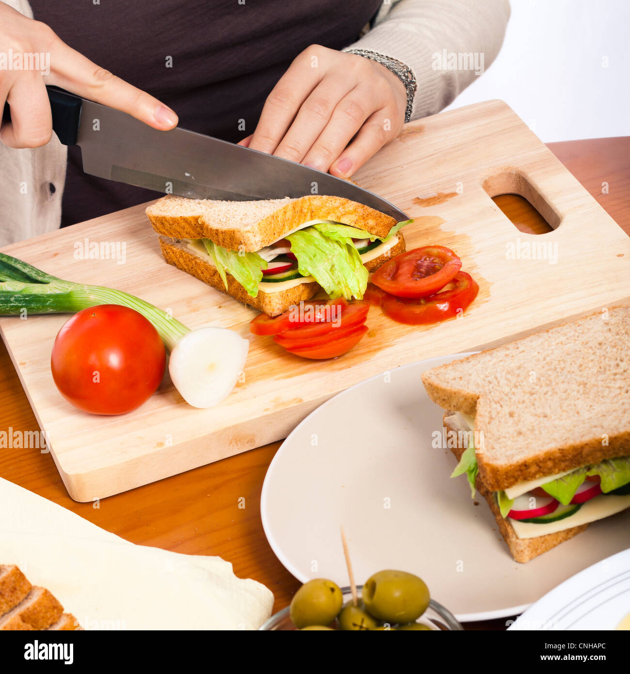 Detail der Küchentisch mit Hacken von Board und Frau Hände Halbierung hausgemachte gesundes Gemüse-Sandwich. Stockfoto