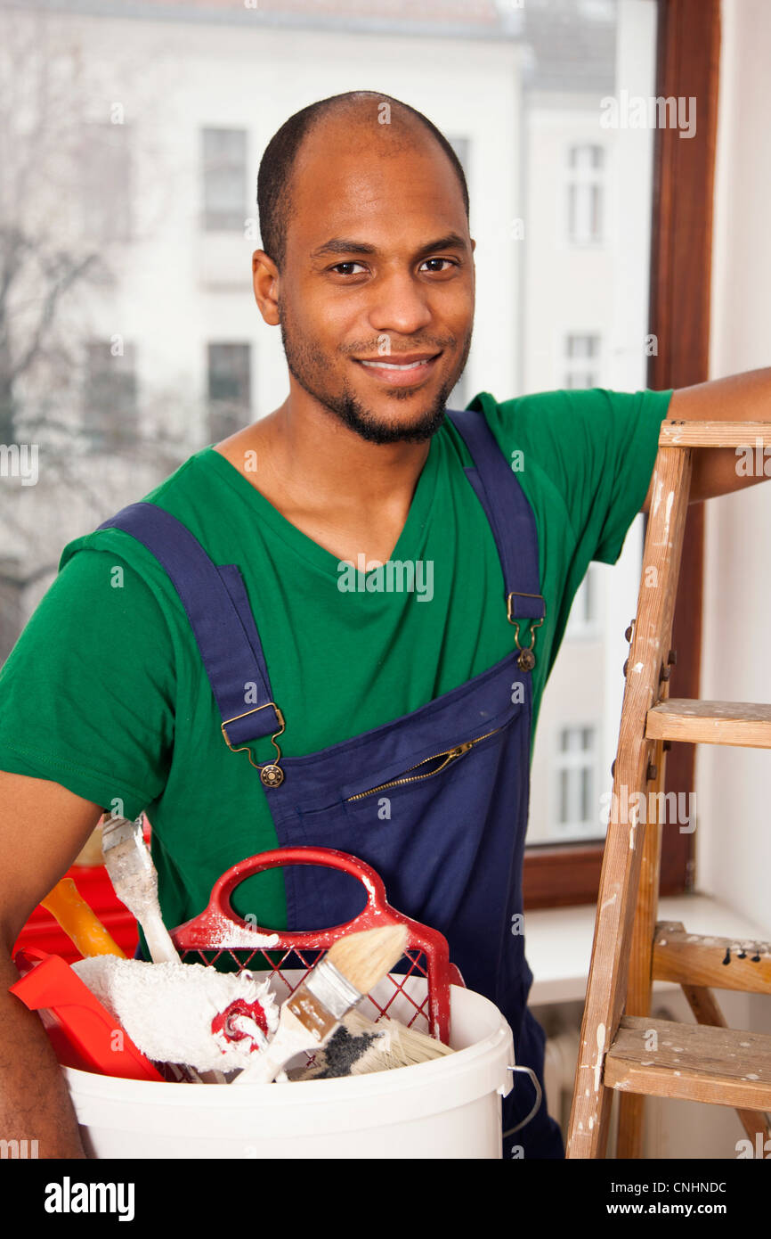 Ein Mann hält einen Eimer Farbe liefert Vorbereitung auf eine Leiter klettern Stockfoto