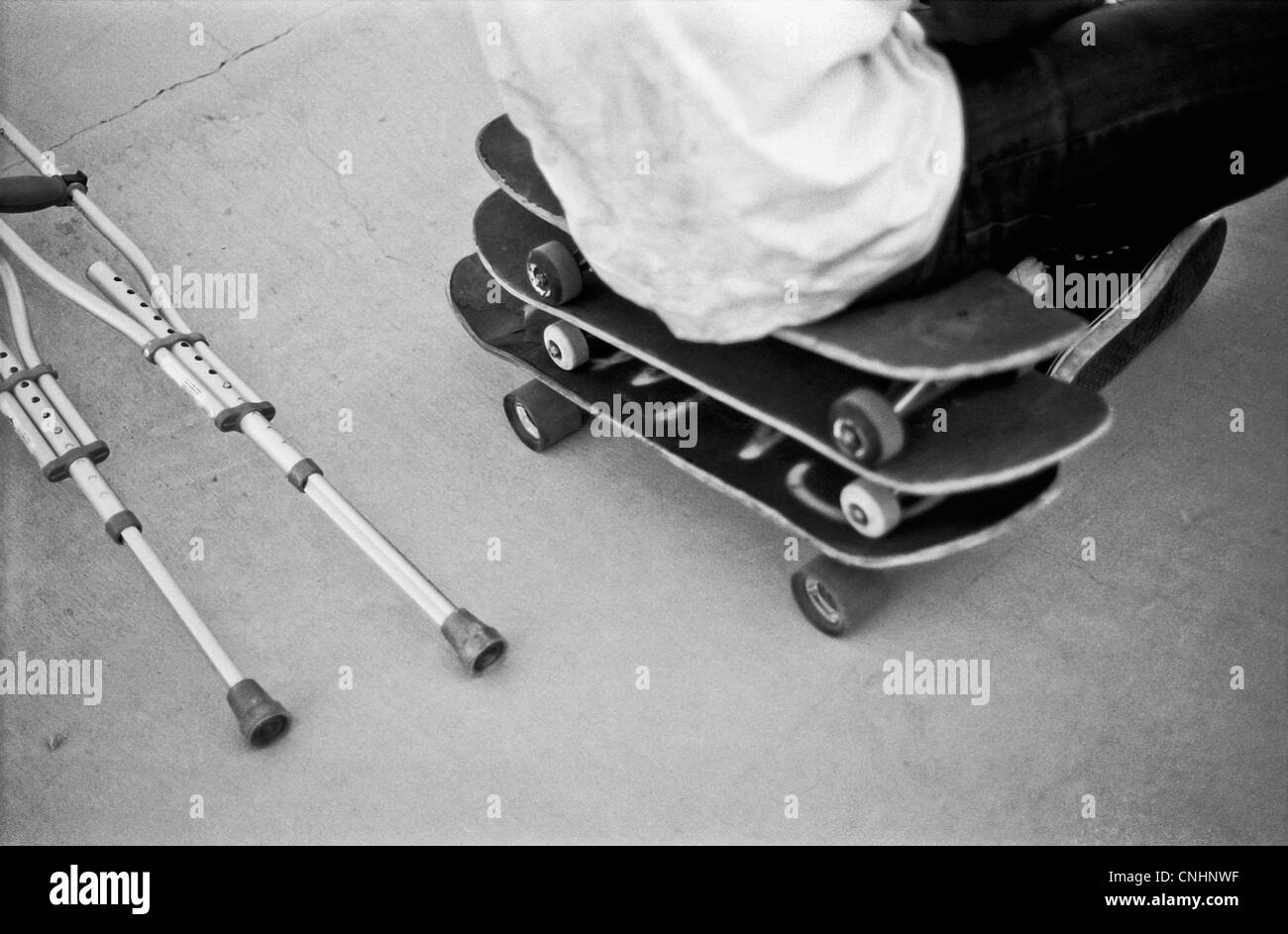 Ein Mann sitzt auf einem Stapel von Skateboards neben Krücken Stockfoto