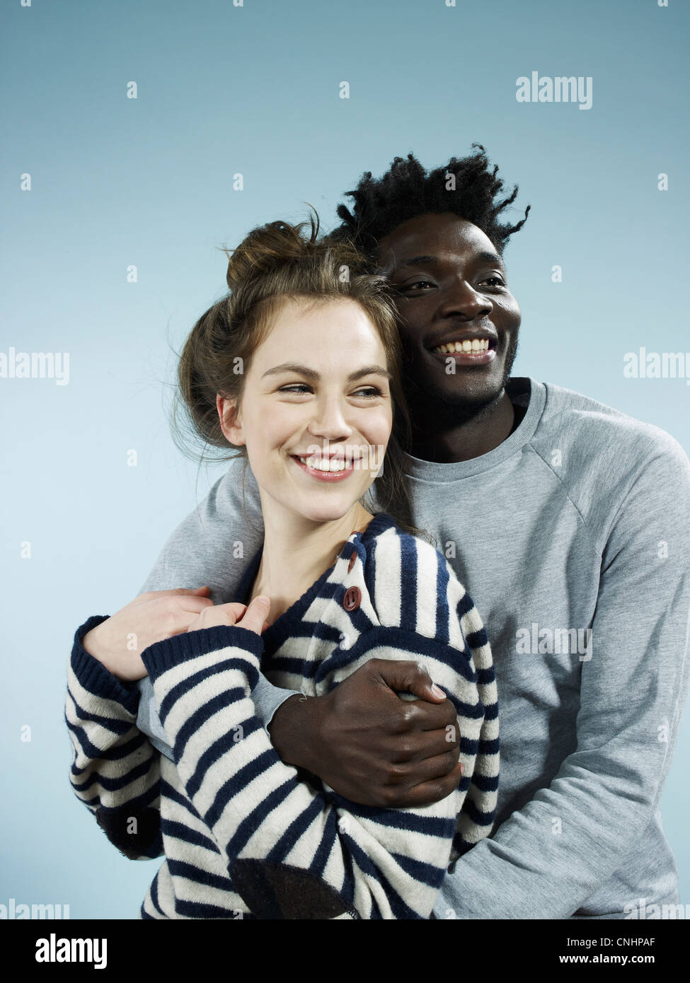 Ein lächelnder junge Mann umarmt seine lächelnde Freundin von hinten Stockfoto