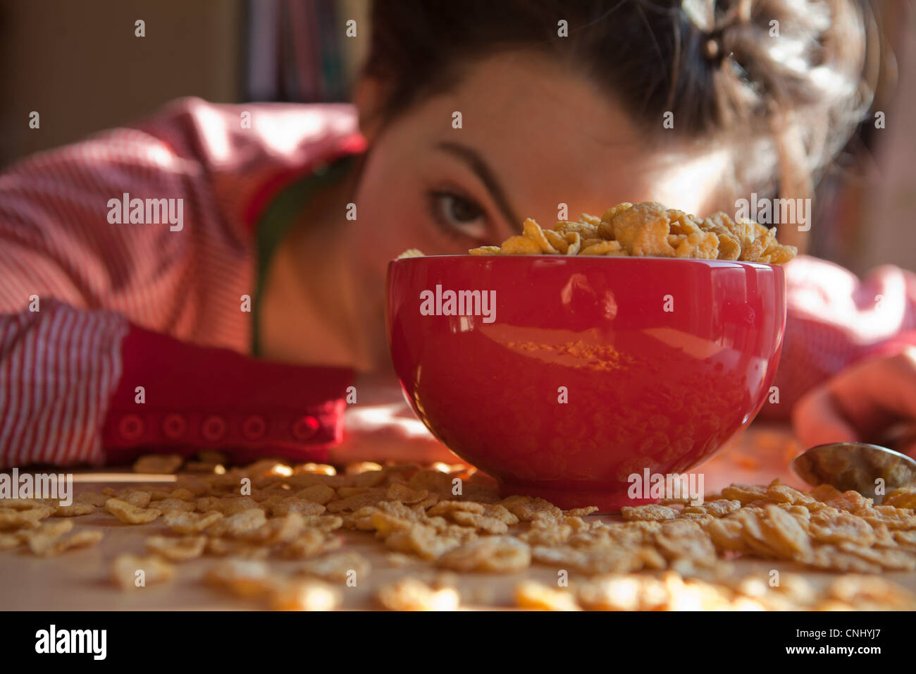 Junge Frau schaut hinter Schüssel und verschüttete Frühstücks-Cerealien Stockfoto