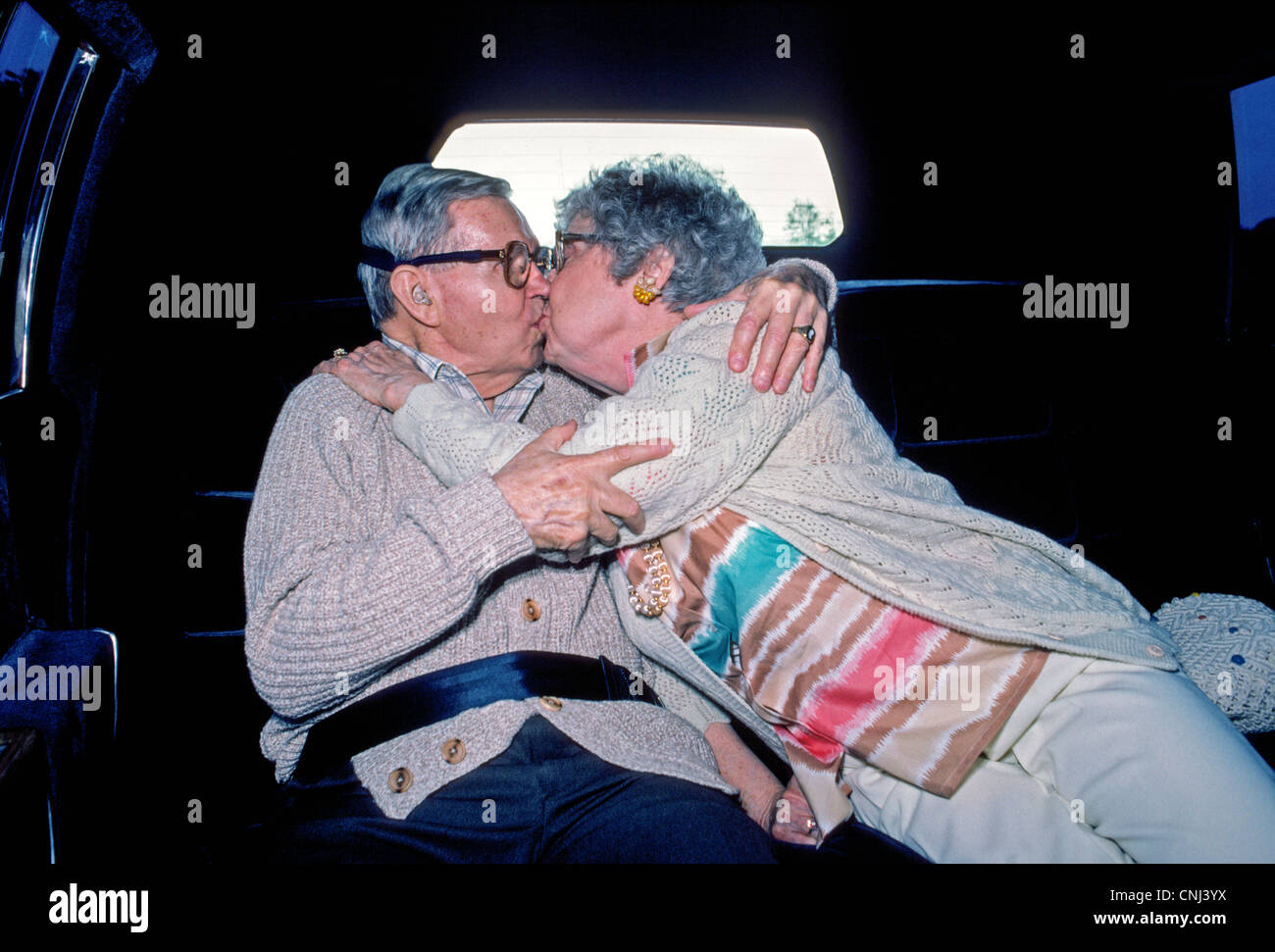 Ein älteres amerikanisches Ehepaar genießen einen Kuss auf dem Rücksitz einer Limousine auf dem Weg zu einer Feier für ihren 50. Hochzeitstag. Stockfoto