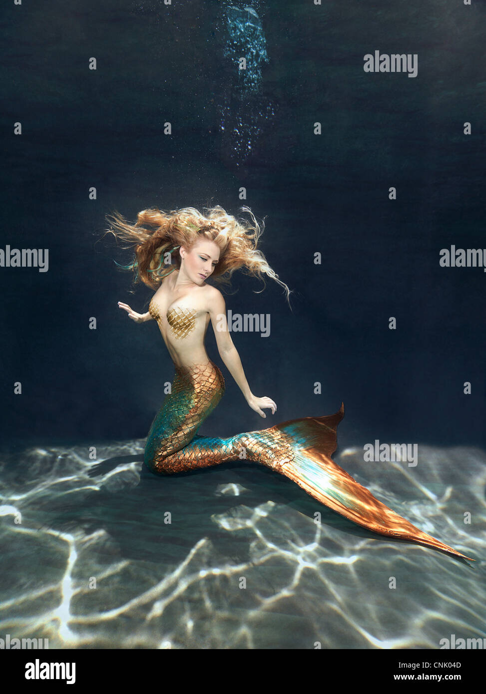 Mermaid Unterwasser kniend auf dem sandigen Boden des Meeres, erreichen für ihre fluke Stockfoto