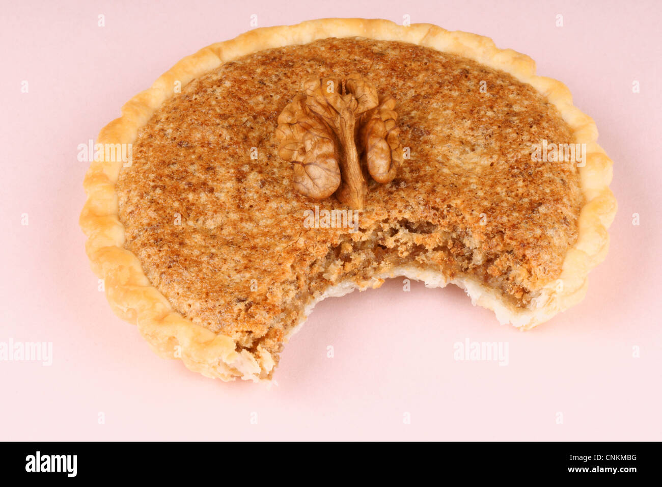 Nahaufnahme einer gebissen Mini-Walnuss-Torte auf einem rosa Papier-Hintergrund Stockfoto