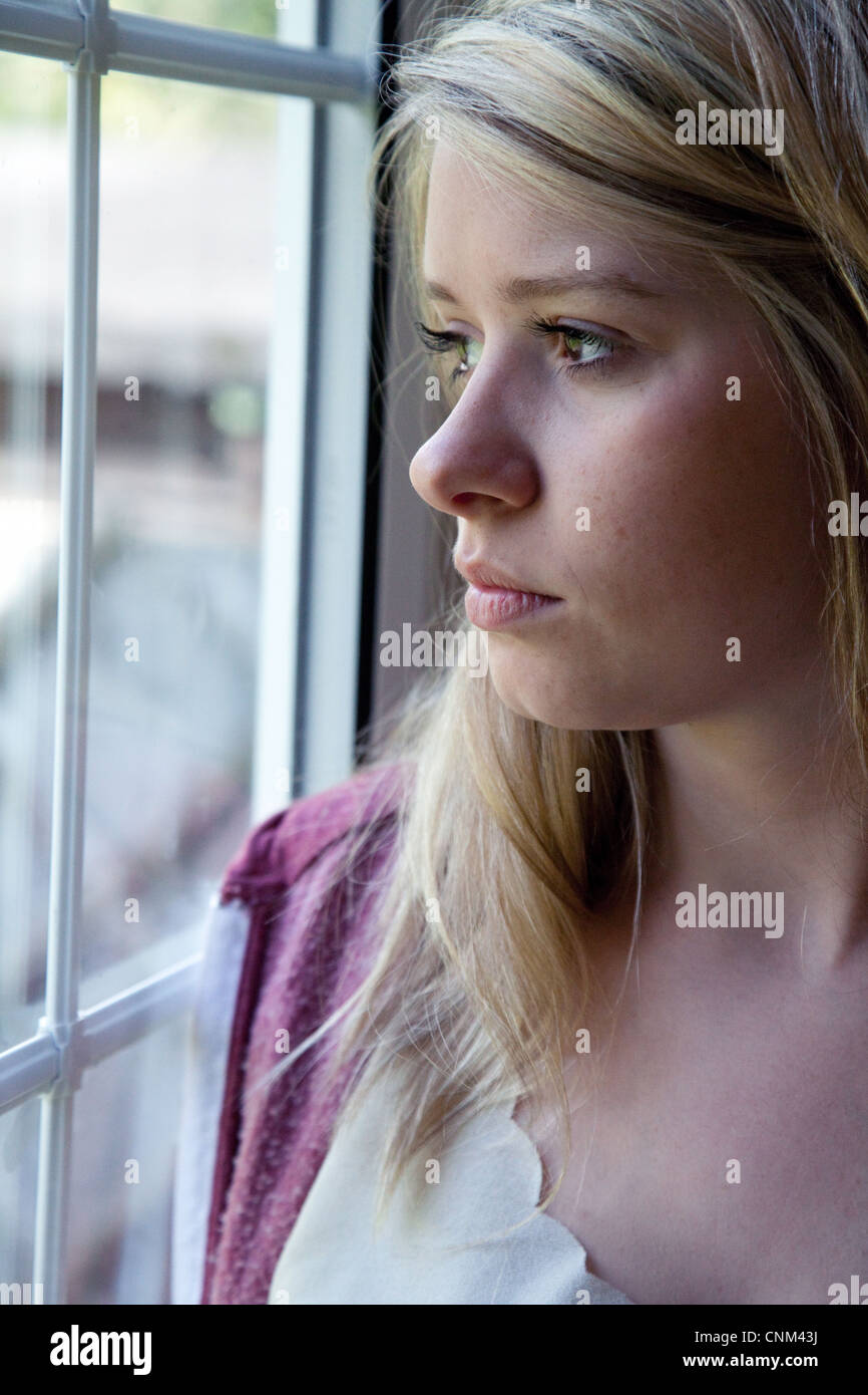 Schöne blonde junge Frau auf der ständigen Suche durch ein Fenster, UK  Stockfotografie - Alamy