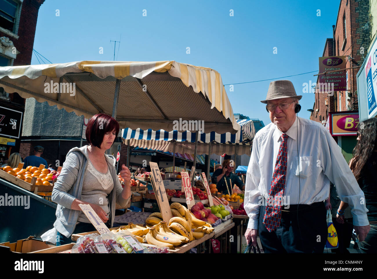 Ein älterer Mann mit einem Hut auf Spaziergänge vorbei an eine Frau an einen Obst und Gemüse Stall in der Moore Street in Dublin Irland Stockfoto
