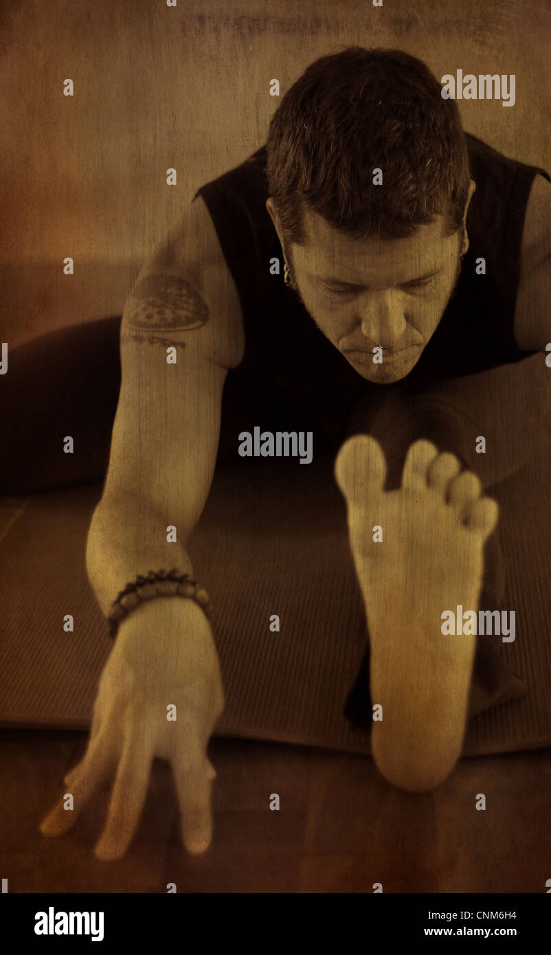 Ein Mann geht in ein sitzen nach vorne beugen Yoga zu praktizieren; eine Version des Janusirsasana. Foto mit Textur & Brauntöne behandelt. Stockfoto