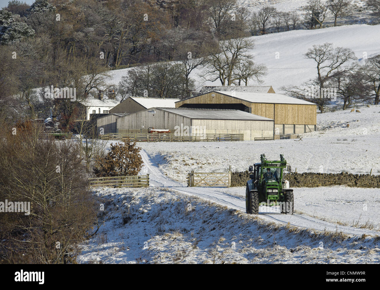 John Deere Traktor entlang Schnee bedeckt Bauernhof Spur Wirtschaftsgebäude im Hintergrund Whitewell Lancashire England november Stockfoto