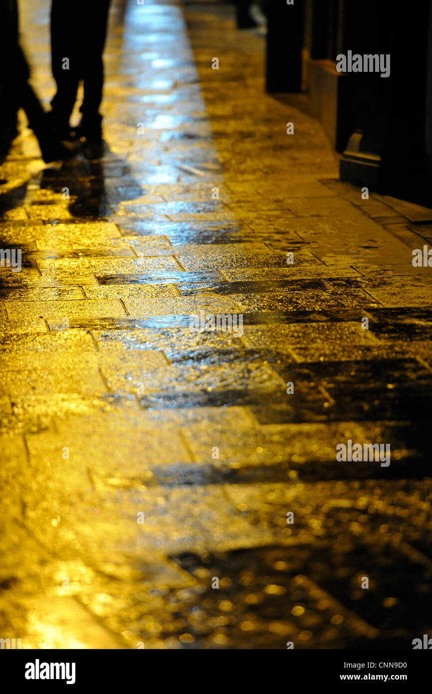Regen durchnässt Pflaster Steinen in der Nacht mit gelben Licht Stockfoto