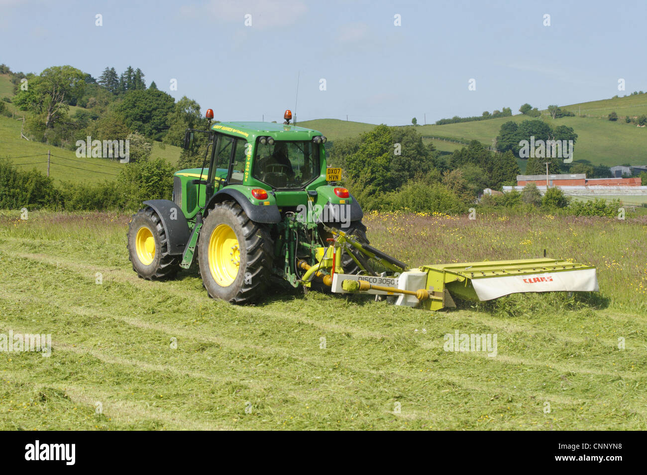 Auftragnehmer mit John Deere Traktor und Claas Mäher mäht Rasen für die Silage auf Bio-Bauernhof, Powys, Wales, Juni Stockfoto