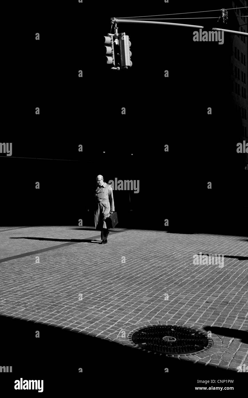 Ein einsamer Geschäftsmann eine kurze Tragetasche ergibt sich aus dem Schatten der Wall Street, New York. Stockfoto