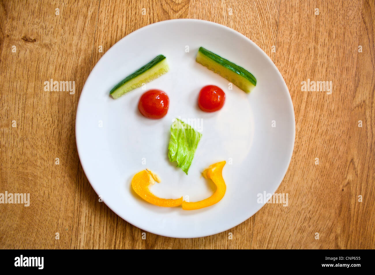 Teller mit gesunden Salat in ein Smiley-Gesicht mit Cherry-Tomaten, Salat, Gurke und gelbe Paprika angezeigt. Stockfoto