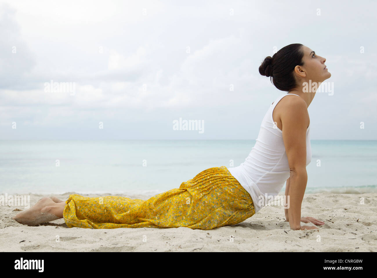 Reife Frau in Kobra-Pose am Strand, Seitenansicht Stockfoto