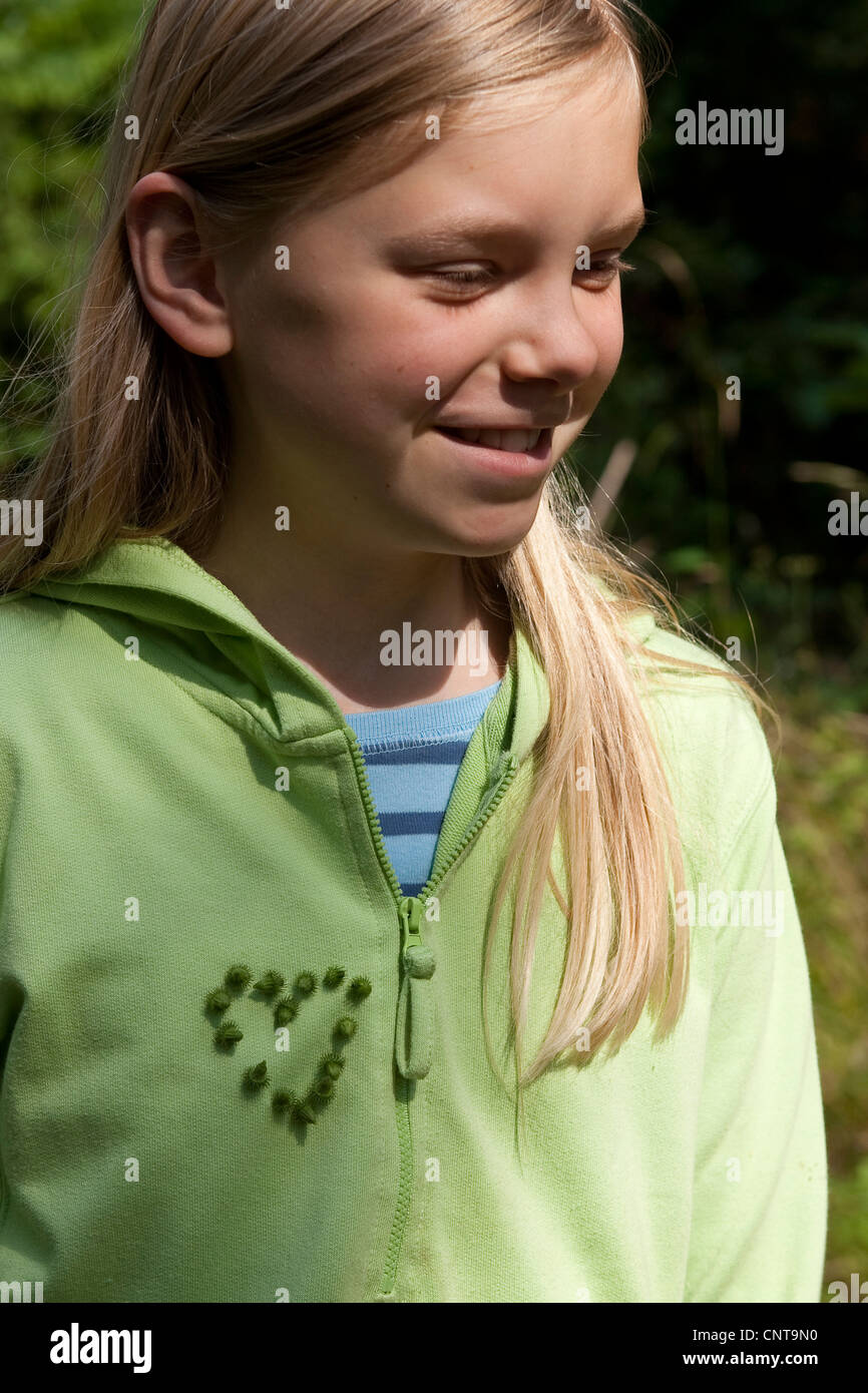 gemeinsamen Klette, weniger Klette (Arctium minus), Mädchen mit festen Burr Früchte auf ihrem Pullover in der Form eines Herzens, Deutschland Stockfoto