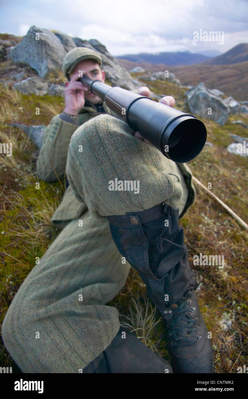 Stalker liegen in den Rasen an einem Berghang auf der Suche nach unten in einem Flusstal durch ein Teleskop, Alladale Wilderness Reserve, Sutherland, Schottland, Vereinigtes Königreich Stockfoto