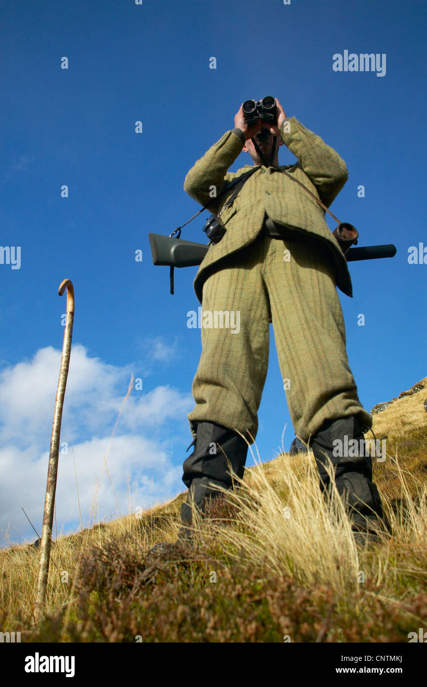 Stalker stehend auf einem Berghang mit Blick auf das Tal durch ein Fernglas, Alladale Wilderness Reserve, Sutherland, Schottland, Vereinigtes Königreich Stockfoto
