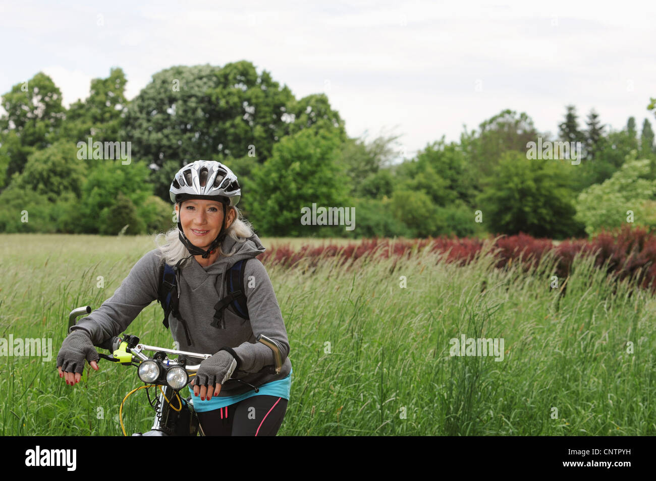 Ältere Frau Reiten Fahrrad auf Landstraße Stockfoto