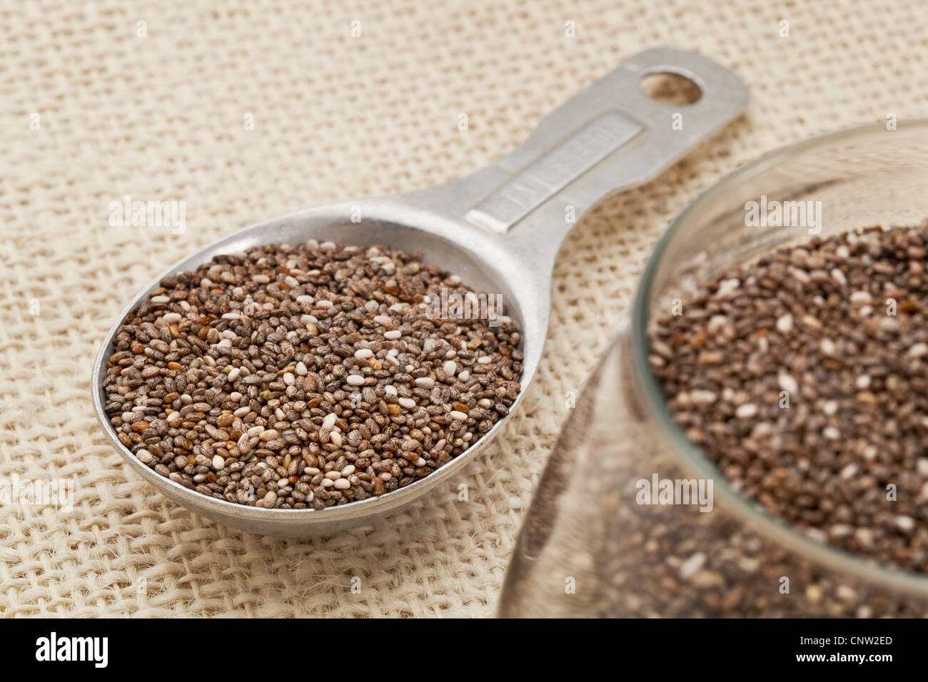 Chia-Samen in Glas und auf der Messung von Aluminium Esslöffel Sackleinen Hintergrund konzentrieren sich auf die Löffel Stockfoto