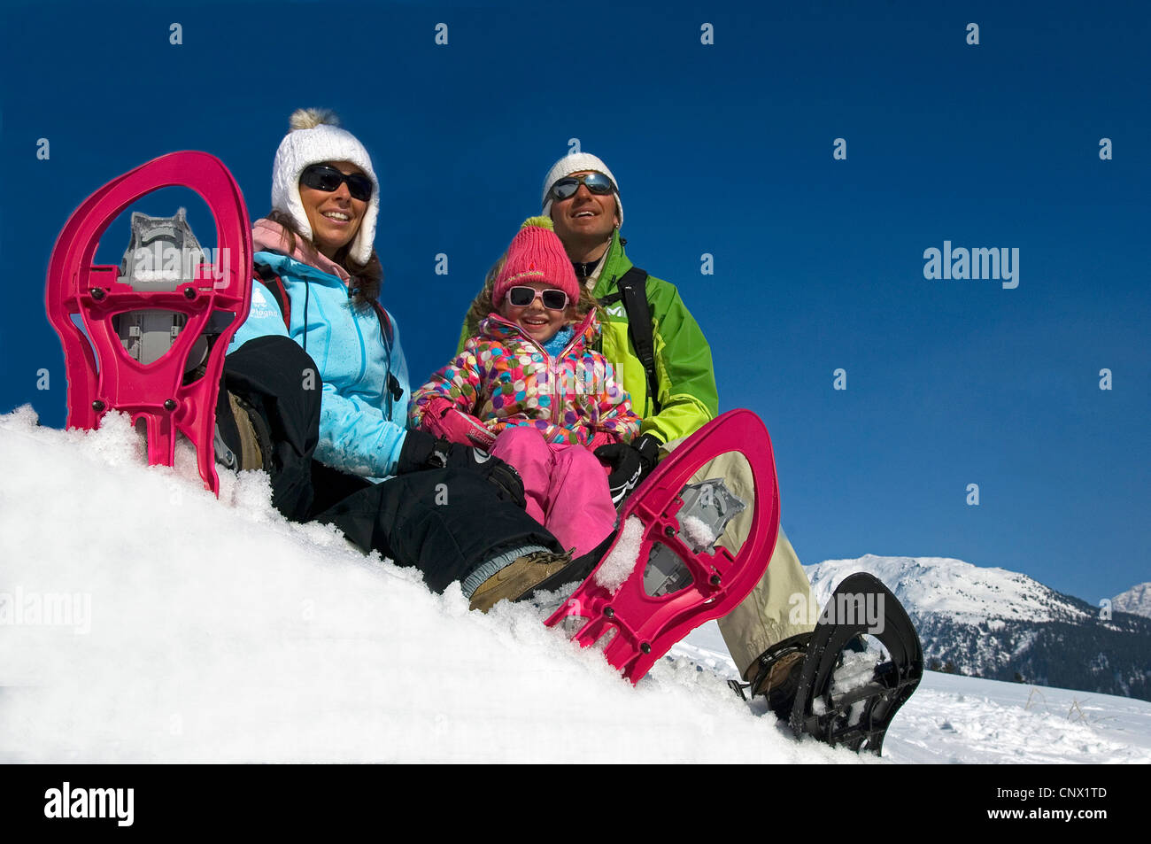 Familie mit drei sitzen im Schnee bei einer Neigung beim Schneeschuhwandern auf Urlaub in den Bergen, Frankreich Stockfoto