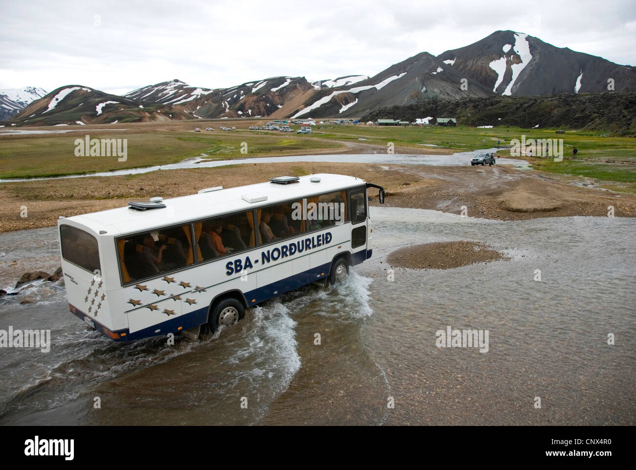 Reisebus Kreuzung Gletscherfluss Joekugilskvisl in einer knappen Ebene vor Bergkette auf dem Weg zum Touristenzentrum, Island, Fjallabak Nationalpark, Landmannalaugar Stockfoto