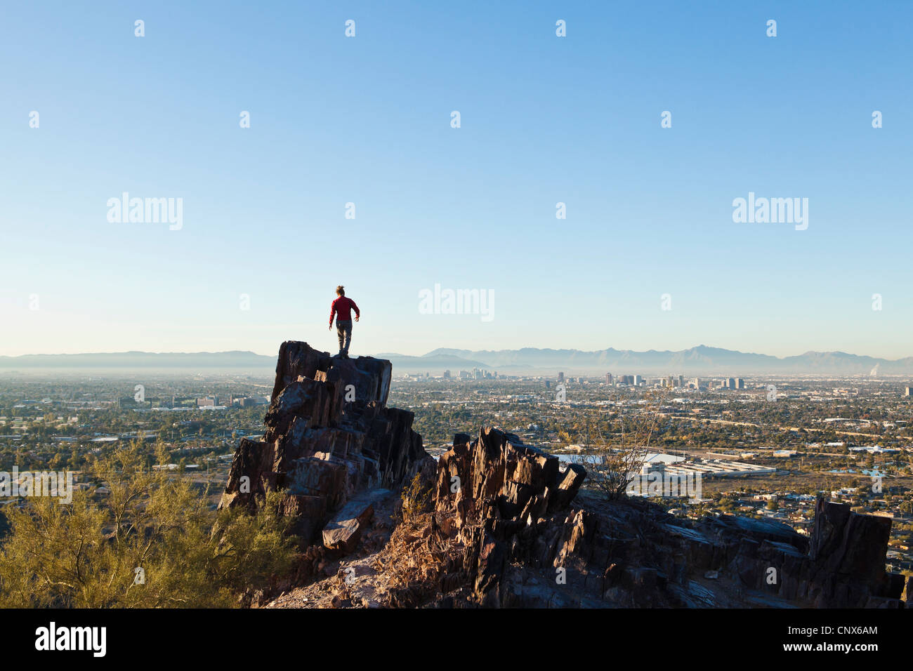 Eine Frau auf einem Felsvorsprung auf Piestewa Gipfel mit Blick auf Phoenix, Arizona / The Valley of The Sun. Stockfoto