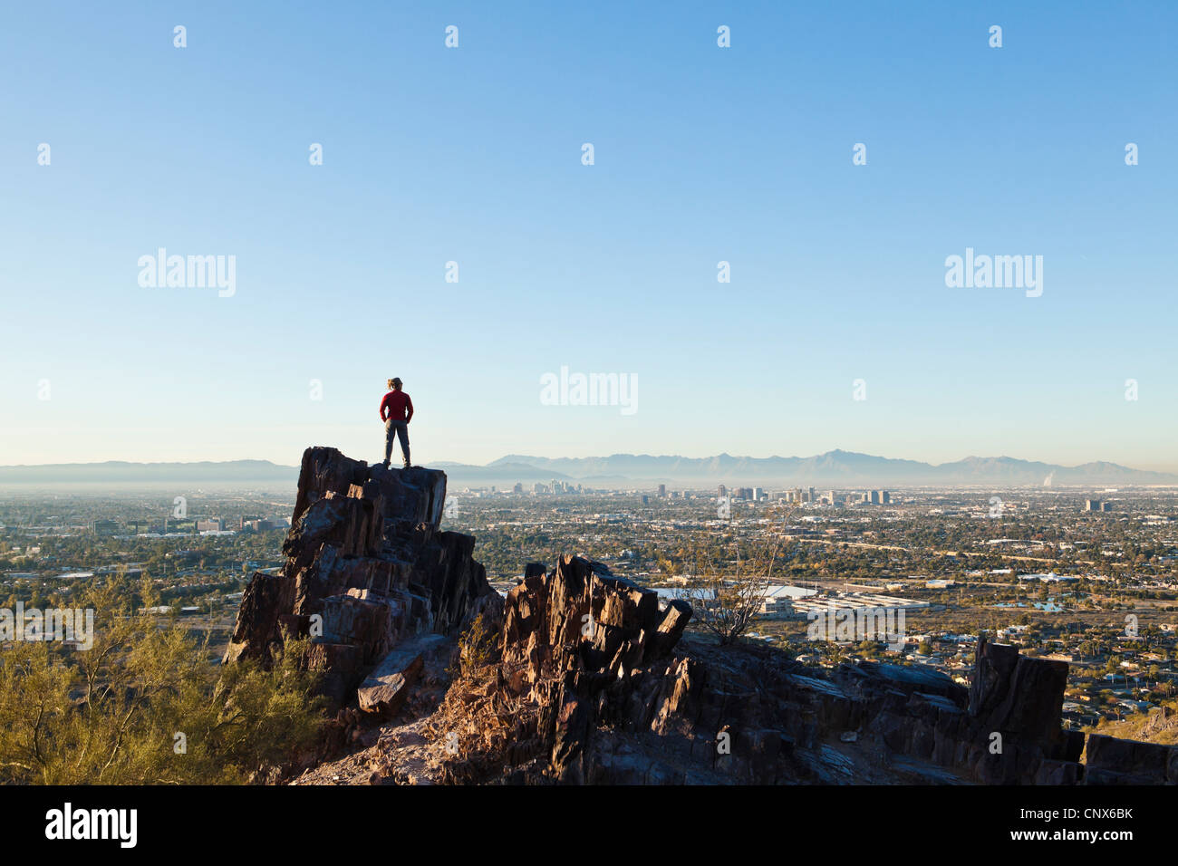Eine Frau steht auf einem Felsvorsprung auf Piestewa Gipfel mit Blick auf Phoenix, Arizona / The Valley of The Sun. Stockfoto