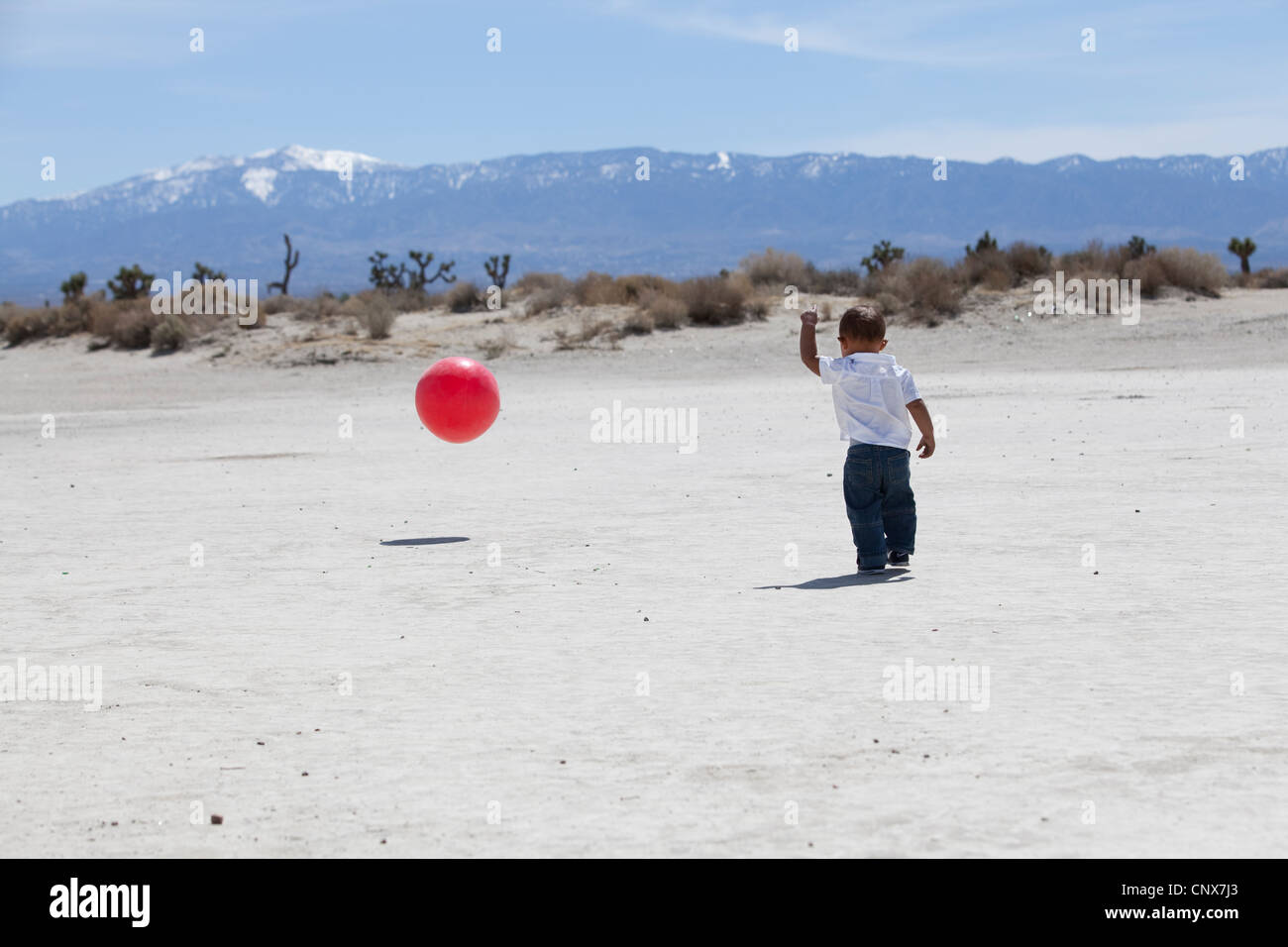 Kind spielt mit einem roten Ball in der Wüste Stockfoto