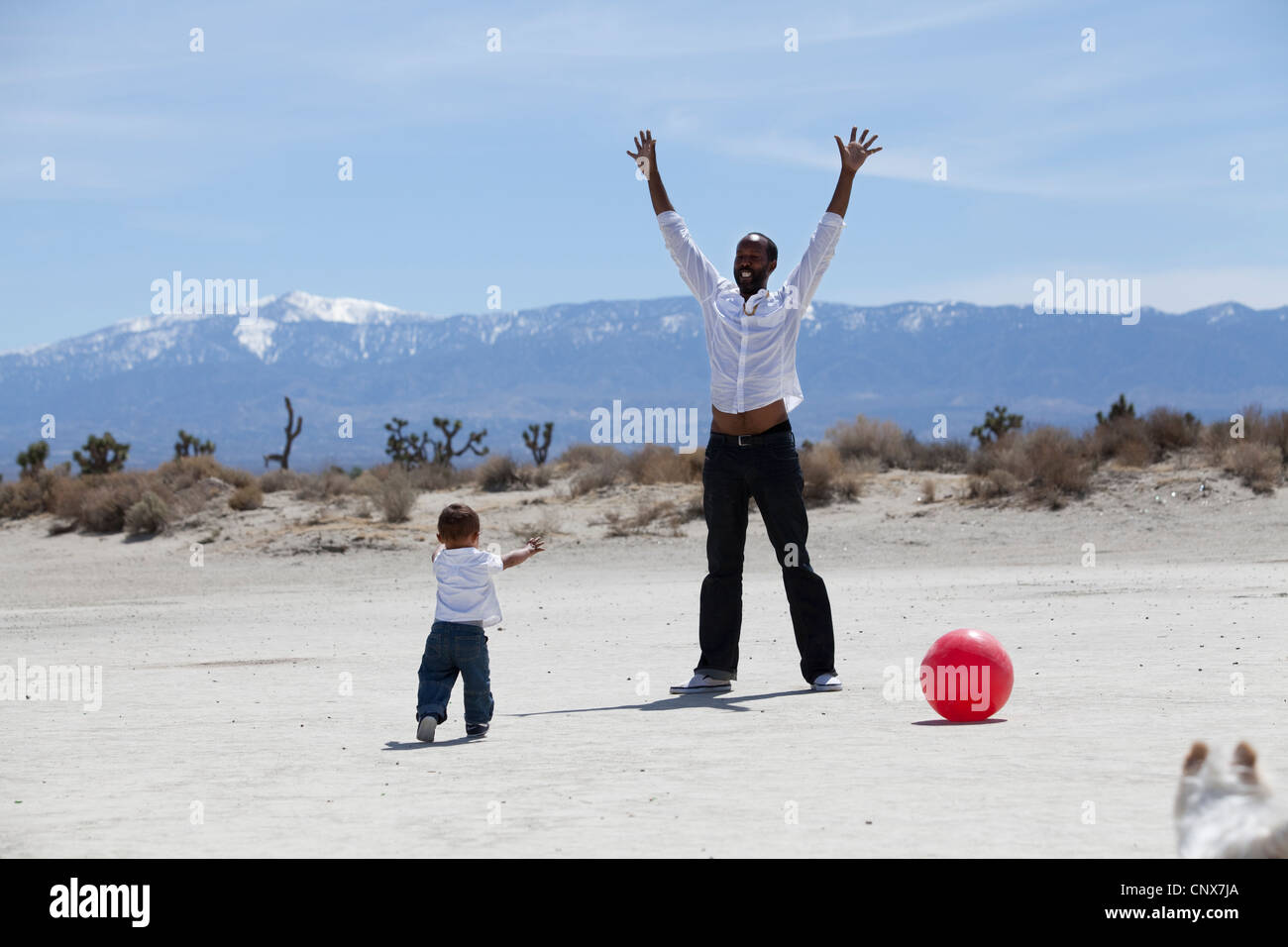 Vater und Sohn in der Wüste mit einem roten Ball spielen Stockfoto